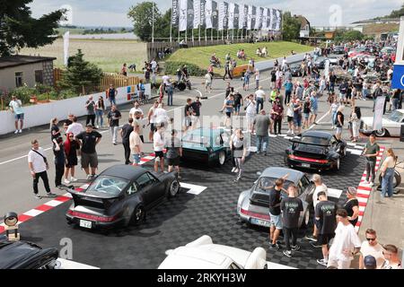 Schleiz, Deutschland. 26. August 2023. Bei der Eröffnung der Motorwelt „Schleizer Dreieck“ laufen die Besucher durch die Ausstellungsfläche. Der Schleizer Dreieck ist Deutschlands älteste Strassenbahn und auch heute noch Austragungsort von Motorsportrennen. Das Museum ist der hundertjährigen Geschichte der Rundstrecke gewidmet. (Gedreht mit Drohne) Credits: Bodo Schackow/dpa/Alamy Live News Stockfoto