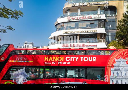 Ein roter Doppeldeckerbus mit offenem Oberdeck, der Touristen eine Stadtbesichtigung von Hanoi bietet, fährt am Kreisverkehr am Ende von Dinh Tien Hoa vorbei an mehreren beliebten Cafés Stockfoto