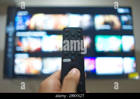 Hand mit TV-Fernbedienung, um TV-Serien von der Streaming-Service-Plattform zu wechseln. Die neue Art, Unterhaltung zu Hause zu genießen. Stockfoto