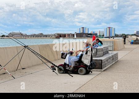 Ein Mann, der an einem Sommertag in Hampshire England UK in einem Behindertenroller vor der Seebrücke von Portsmouth sitzt und angeln kann Stockfoto