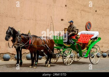 Marrakesch, Marokko, 8. April 2023. Ein marokkanischer Mann sitzt vor einer Pferdekutsche und wartet auf die Kunden in der Nähe einer alten Mauer in Marrakesch. Stockfoto