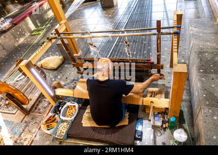 Ein Webmeister betreibt die Webmaschine in der Weberei und Werkstatt Naseej im Dorf Bani Jamra in Bahrain Stockfoto