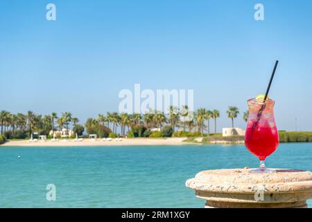 Ein Glas Rotgetränk, Limonade mit Zitrone und Stroh gegen die Bahrain Bay, die Skyline des Nahen Ostens Stockfoto