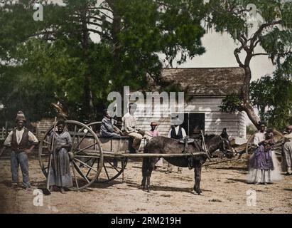 Das Foto zeigt eine Gruppe afroamerikanischer Sklaven, die sich um einen Pferdewagen mit einem Gebäude im Hintergrund auf der Cassina Point Plantage von posierten Stockfoto