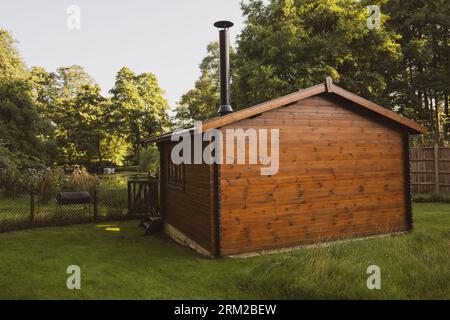 Ein hölzernes Sommerhaus mit einem Kamin aus Holz überblickt einen kleinen See in einem privaten Garten in Thetford, Norfolk, England Stockfoto