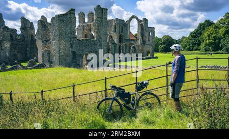 Ein Mann steht in der Nähe seines Fahrradfahrrads und genießt den Blick über die Ruinen der Castle Acre Priory in Castle Acre Norfolk England Stockfoto