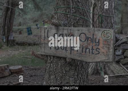 Schild aus einer Holzplanke, die an einem Baum befestigt ist, auf dem steht, dass nichts als Fußabdrücke hinterlassen wird Stockfoto