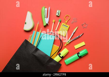 Paper bag with colorful stationery on red background Stock Photo