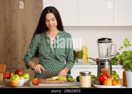 Junge Frau schneidet Banane für Smoothie in der Küche Stockfoto