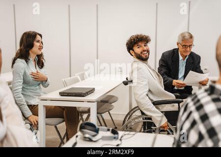 Generationsübergreifende Gruppe von Geschäftsleuten, die im Klassenzimmer eine geschäftliche Präsentation halten. Behinderter männlicher Geschäftsmann lächelt und posiert für die Stockfoto