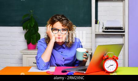 Zurück zur Schule. Müde Lehrerin trinkt Kaffee im Klassenzimmer. Überarbeiteter Student an einer Universität, der sich auf die Prüfungssitzung vorbereitet. Schulferien Stockfoto