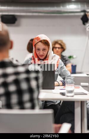 Glückliche, positive, erfolgreiche, glamouröse Geschäftsfrau, die bei der Arbeit auf dem Laptop arbeitet, versammelte sich mit ihren Teamkollegen am Tisch. Vorderansicht Foto Stockfoto