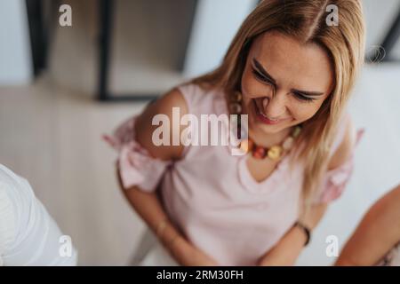 Schöne Geschäftsfrau mittleren Alters oder leitende Geschäftsfrau, die in einer positiven Atmosphäre in einem modernen Firmenbüro arbeitet. Sie unterhält sich lustig mit ihrem Tee Stockfoto