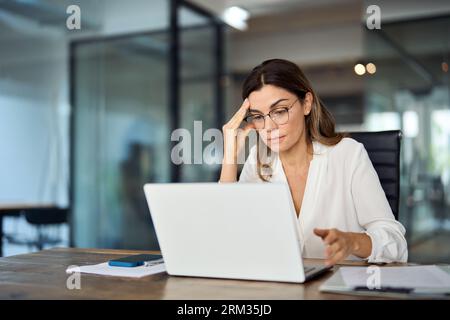 Besorgte, müde, reife Geschäftsfrau mit Brille und Kopfschmerzen bei der Arbeit. Stockfoto