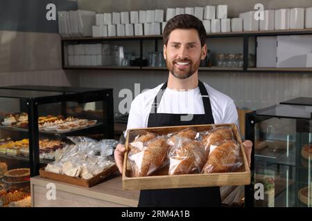 Glücklicher Verkäufer, der ein Tablett mit leckeren Croissants in der Bäckerei hält Stockfoto