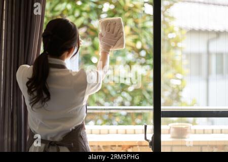 Asiatische Frau putzt das Wohnzimmer-Fenster Stockfoto