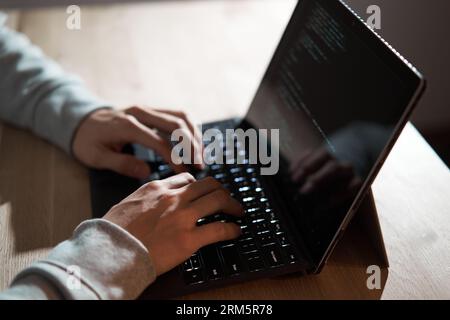 Männlicher Hacker schlägt Text auf einem Laptop Stockfoto