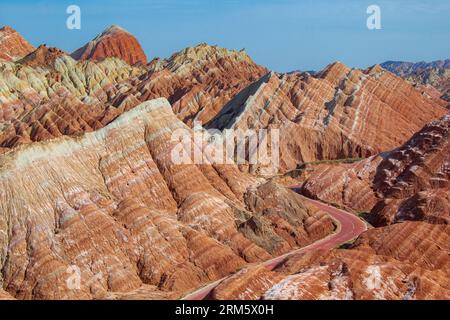 Kurvige Straße durch die bunten Regenbogenberge. Die chinesische Landschaft auf der Seidenstraße. Wunderschöner Sonnenuntergang im Zhangye Danxia National Geological Park, Gan Stockfoto