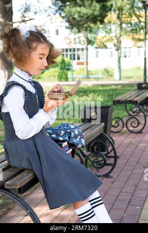 Mädchen mit Rucksack, das Sandwich in einer Sandwichbox in der Nähe der Schule isst. Ein schneller Snack mit einem Brötchen, ungesundes Essen, Mittagessen aus der Schule. Zurück zur Schule. Stockfoto