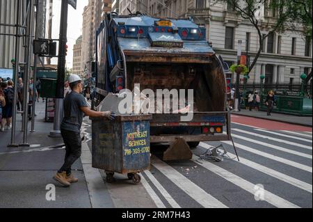 New York, New York, USA, 07-18-2023 Sanitärarbeiter Rollen Mülltonnen, um den Müllwagen auf der geschäftigen Manhattan, New York City Street zu öffnen. Natürlich aufgenommen Stockfoto