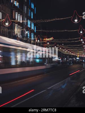Eine vertikale Straßenbahnlinie, die nachts auf der Straße von Damrak in Amsterdam, Niederlande, fährt Stockfoto