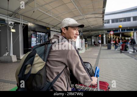 Mann, der den Gepäckwagen schiebt und vor dem Flughafen spaziert. Nicht erkennbare Passagen im Hintergrund. Stockfoto