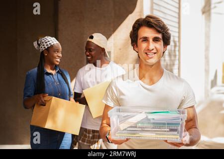 Glücklicher junger Mann, der eine Box mit Notizblöcken im Freien hält Stockfoto