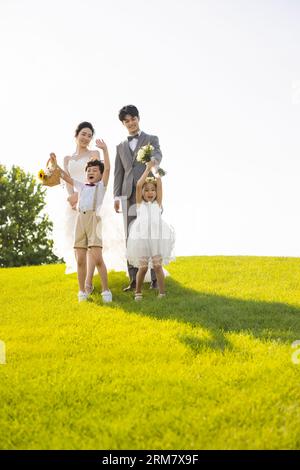 Chinesische Braut und Bräutigam spazieren durch einen Park mit Blumenmädchen und Ringträgerin Stockfoto