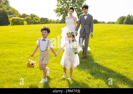 Chinesische Braut und Bräutigam spazieren durch einen Park mit Blumenmädchen und Ringträgerin Stockfoto