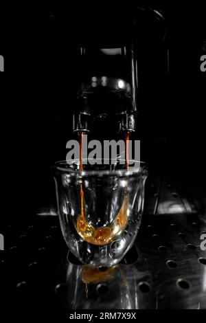 Kaffee, der aus dem doppelten Kaffeeauslauf fällt und eine Glasschale mit Schaum und Blasen aus einer automatischen Espressomaschine füllt, mit schwarzem und weißem Hintergrund Stockfoto