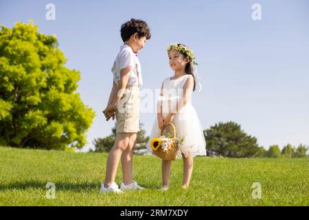 Niedliches Blumenmädchen und Ringträgerin, die auf dem Gras spielen Stockfoto