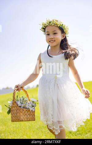 Niedliches Blumenmädchen, das auf dem Gras spielt Stockfoto
