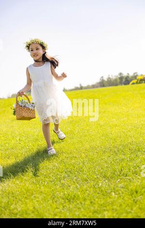 Niedliches Blumenmädchen, das auf dem Gras spielt Stockfoto