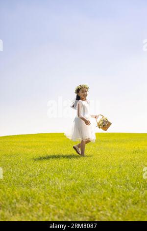 Niedliches Blumenmädchen, das auf dem Gras spielt Stockfoto