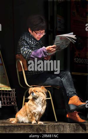 NINGBO, 23. März 2014 (Xinhua) - Ein Hund genießt Sonnenschein neben einer Frau, die Zeitung auf einer Straße in Ningbo, einer Hafenstadt in der ostchinesischen Provinz Zhejiang, liest, 23. März 2014. (Xinhua/Hu Xuejun) (lfj) CHINA-ZHEJIANG-NINGBO-LIFE (CN) PUBLICATIONxNOTxINxCHN Ningbo 23 2014. März 2014 XINHUA ein Hund genießt Sonnenschein neben einer Frau, die Zeitung AUF einer Straße in Ningbo liest, einer Hafenstadt in Ostchina Stockfoto