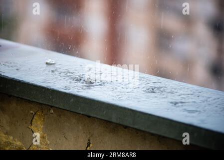 Tagesaufnahme von Regentropfen, die vom grauen Himmel auf die nasse Oberfläche eines Balkongeländes fallen und Wellen im stillen Wasser erzeugen, Belgrad, Serbi Stockfoto