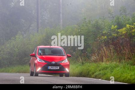 Whittlebury, Northants, UK - 26. August 2023: Rotes 2016 Toyota Aygo Auto, das an einem feuchten und nebligen Morgen auf einer englischen Landstraße fährt. Stockfoto