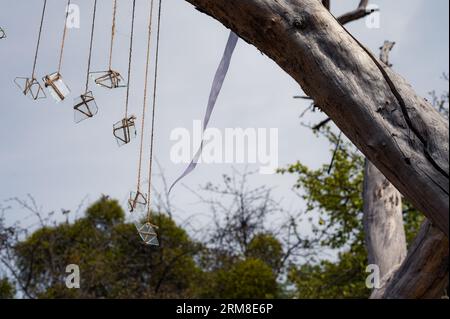 Gruppe von Glasstücken auf den Schnüren und weißem Band mit dem Himmel und Holz als Hintergrund. Abstraktes Dekor Stockfoto