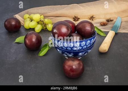 Ein wunderschönes Stillleben mit Reifen Kirschen auf blauen Porzellanschüsseln neben einigen weißen Trauben und einem hellen Tuch auf einer grauen Oberfläche Stockfoto