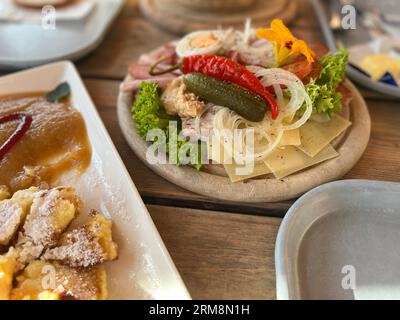 Köstliche Frühstücksoptionen mit rustikalem Aufschnitt, Käse und Gemüse sowie einem süßen österreichischen Kaiserschmarrn mit Apfelsauce Stockfoto