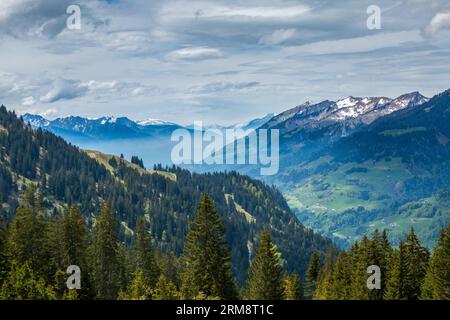 Frühlingssonne, die Wälder, Bauernhöfe und die teilweise verschneiten Berge des Großen Walsertals in den österreichischen Alpen, Vorarlberg, erleuchtet Stockfoto