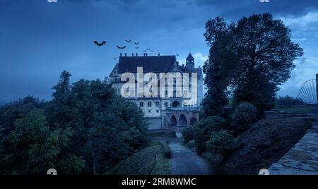 Spukschloss in der Halloween-Nacht, altes gruseliges Herrenhaus mit Fledermäusen in der Abenddämmerung. Blick auf die gruselige dunkle Burg in der blauen Dämmerung. Düstere Szene zum Thema Hallowen. Stockfoto