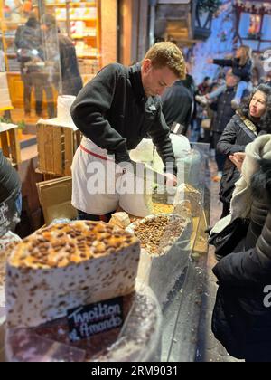 Colmar, Frankreich - 26. November 2022: Man schneidet große Nougatscheiben vor Kunden an einem Stand im Freien auf dem Weihnachtsmarkt von Colmar Stockfoto