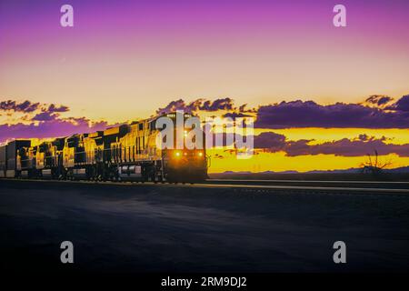 Fesselnde Blue-Hour-Fotografie von BNSF 6583, die sich in östlicher Richtung entlang der historischen Route 66 an der Goffs Road in der Mojave-Wüste bewegt, ergänzt durch eine warme Sonne Stockfoto