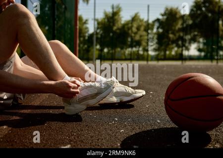Cropped image of sportsman tying shoelaces sitting on basketball court Stockfoto
