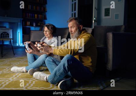 Seniorenpaar sitzt auf dem Boden und spielt Videospiele auf der Konsole Stockfoto