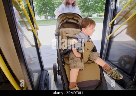 Das Kind steigt mit seiner Mutter in den Bus, bereit einzusteigen und einen Platz zu finden. Junge im Alter von zwei Jahren (zwei Jahre) Stockfoto