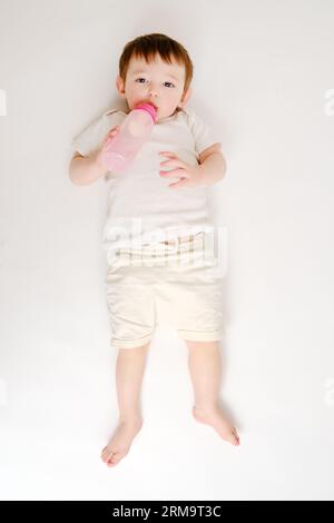 Happy Baby trinkt Milch aus der Flasche auf weißem Studiohintergrund. Ruhendes Kind isst Formel. Kind etwa zwei Jahre alt (ein Jahr neun Monate) Stockfoto