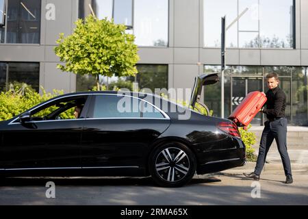 Chauffeur packt einen Koffer in ein Luxusauto Stockfoto