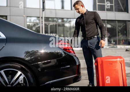 Chauffeur packt einen Koffer in ein Luxusauto Stockfoto